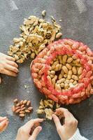 Mesh bag with inshell peanuts and two girls in the background are peeling nuts at the table. Lifestyle. Top and vertical view photo