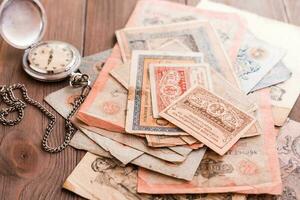 A stack of old outdated ruble bills and a frayed watch on a chain on a wooden table photo