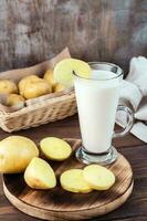 Alternative vegetable vegan potato milk in a glass and potato tubers side by side on a wooden table. Vegetarian food. Vertical view photo