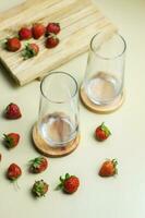 close up of strawberries and two clear glasses on a pastel yellow background photo