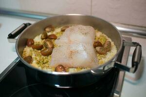 cerca arriba de un Cocinando maceta con arroz, merluza y Cereza Tomates foto