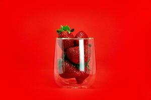 Strawberries in a glass transparent beaker with highlights close-up on a red background. Romantic background. photo