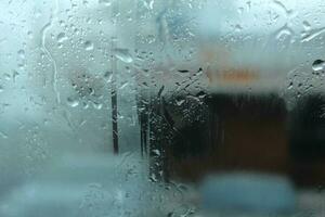 un de cerca de el mojado vaso ventana de un motor vehículo, con gotas de lluvia y nieve que cae en el congelación interior antecedentes. foto