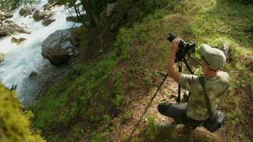 fotografo con telecamera attrezzatura su il montagna fiume riva video