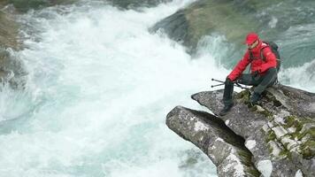Backpacker with Nordic Walking Poles Relaxing on the River Boulder. Slow Motion Footage video