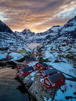 rojo pescar cabañas en lofoten Noruega en puesta de sol por zumbido, nieve montañas foto