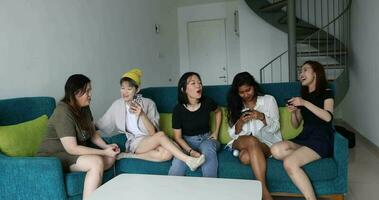 ung asiatisk kvinna grupp prata skvaller chatt sjunga dryck Skål fest roligt njut av full trött resten rolig ansikten uttryck på blå levande rum soffa video
