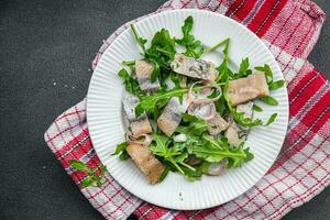 herring pieces pickled onion, green arugula leaves meal food snack on the table copy space food background rustic top view  pescatarian diet photo