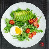 avocado salad poached egg, arugula, tomato, green salad leaves healthy meal food snack on the table copy space food background rustic top view keto or paleo diet veggie photo