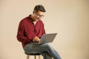 Simple young freelancer sitting working on laptop pc computer looking isolated on bright colored wall, studio photo background.