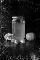 A photo that has a honey container, some decorations, and some fruits. This image is made in a black-and-white pattern