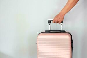 Male hand holding peach suitcase on gray background. Vacation concept photo