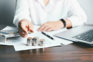 Saving money concept preset by female hand putting money coin stack growing business. Asian woman checking bills, taxes, bank account balance and calculating credit card expenses. photo