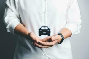 Business woman's hand protecting black icon car on desk. Planning to manage transportation finance costs. Concept of car insurance business, saving buy - sale with tax and loan for new car. photo