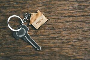 House key on a house shaped keychain resting on wooden floorboards concept for real estate renting property. House model and key in house door. Real estate agent offer house, property insurance. photo