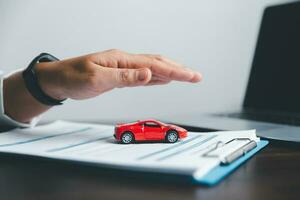 Business woman's hand protecting red toy car on desk. Planning to manage transportation finance costs. Concept of car insurance business, saving buy - sale with tax and loan for new car. photo