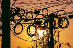 Electricity messy wires on pole. Silhouette at sunset photo