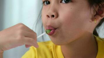 linda pequeño niña comiendo chupete. gracioso niño con pirulí caramelo. niño comiendo dulces video