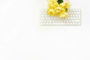 Flat lay blogger or female freelancer workspace. An office white Desk with a keyboard and a bunch of yellow spring tulips on it. Copy space. A gift at the workplace photo