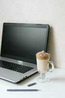 Dalgona coffee in a clear mug, Notepad, pen and computer on the table. Top view. Coffee break at the workplace of a blogger or freelancer photo