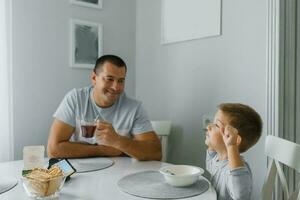 contento papá y su pequeño hijo son teniendo desayuno en el cocina foto