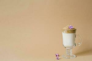 Beautiful dalgon coffee drink with foam in a transparent Cup and lilac flowers on a beige background. Copy space photo