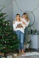 dos hermosa rubia hermanas teniendo divertido, consiguiendo Listo para el celebracion, decorando el Navidad árbol. un brillante celebracion de mejor amigos vestido en calentar invierno suéteres foto
