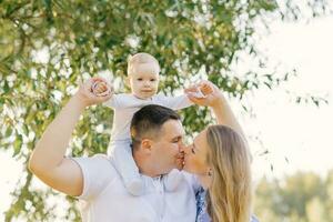 A European family in the park on a summer day. Mom, dad and little son in their arms. Parents kiss each other photo