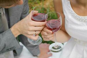 el novia y novio con Boda anillos sostener lentes de rojo vino en su manos foto