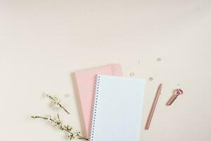 A blank notebook sheet with a sprig of white apple blossoms, a pink notebook and a pink pen on a beige background. Spring concept for a blog with copy space photo