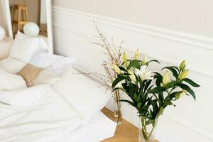 White lily flowers in a vase, tree branches in a vase near the bed. Details of the interior decor of the house photo