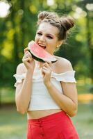 A smiling girl holds a sweet watermelon in her hands and smiles while biting it photo