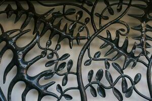 A metal grill in the form of a tree branch with black leaves on a light gray background. Original background for copy space. photo