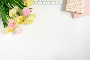 Springtime flat fly with keyboard, notebooks, bunch of pink tulips on a light background. Spring concept for a blog. Greeting Card for Valentine's Day or Mother's Day photo