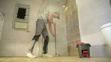 caucásico hombres en su 30s trapear y limpieza baño cerámico loseta piso. video