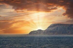 View from the sea to the West Cape in Norway at sunset. Sun shines over the rocks photo