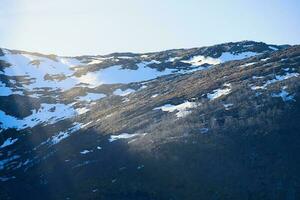 nieve cubierto montaña por el fiordo en Noruega. solamente un pocos arboles Entre el rocas foto