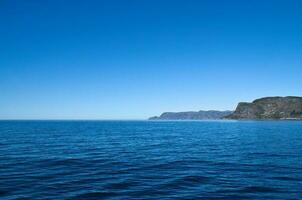 ver desde el mar a el Oeste capa en Noruega en luz solar. olas y rocas foto