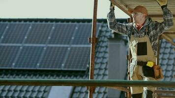 construcción trabajador en un andamio mirando alrededor. casa techo con solar paneles en un antecedentes. video