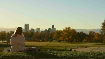 Frau Sitzplätze auf ein Gras Innerhalb Denver Stadt Park und genießen szenisch Sonnenuntergang video