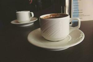 little white cup with hot black coffee on a brown table photo
