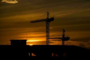 pintoresco puesta de sol con nubes en el cielo en el ciudad con construcción grúas, foto