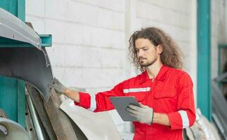 mecánico hombre con digital tableta inspeccionando coche partes valores en garaje depósito, joven mecánico trabajando en auto reparar tienda foto