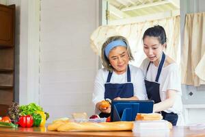 madre asiática mayor e hija de mediana edad cocinando juntas en la cocina foto