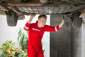 Auto mechanic working in garage, Technician man working in auto service with lifted vehicle, Car repair, and maintenance photo