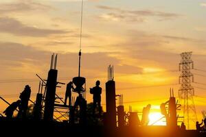 silueta de ingeniero y trabajador equipo comprobación proyecto a edificio sitio fondo, construcción sitio con puesta de sol en noche hora antecedentes foto