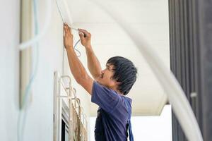 técnico hombre instalando aire acondicionamiento en un cliente casa, joven reparador fijación aire acondicionador unidad, mantenimiento y reparando conceptos foto