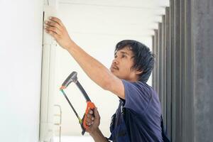 artesano trabajador aserradura un tubo, técnico hombre instalando un aire acondicionamiento en un cliente casa, joven reparador fijación aire acondicionador unidad, mantenimiento y reparando conceptos foto