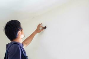 técnico hombre instalando aire acondicionamiento en un cliente casa, electricista montaje el alambres dentro muro, reparador fijación aire acondicionador unidad, mantenimiento y reparando conceptos foto