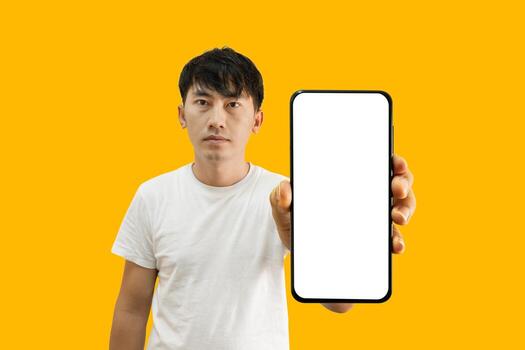 Asian Man Holding Smartphone With White Empty Screen On Yellow Background. Cellphone display Mockup for Mobile App Advertisement. photo